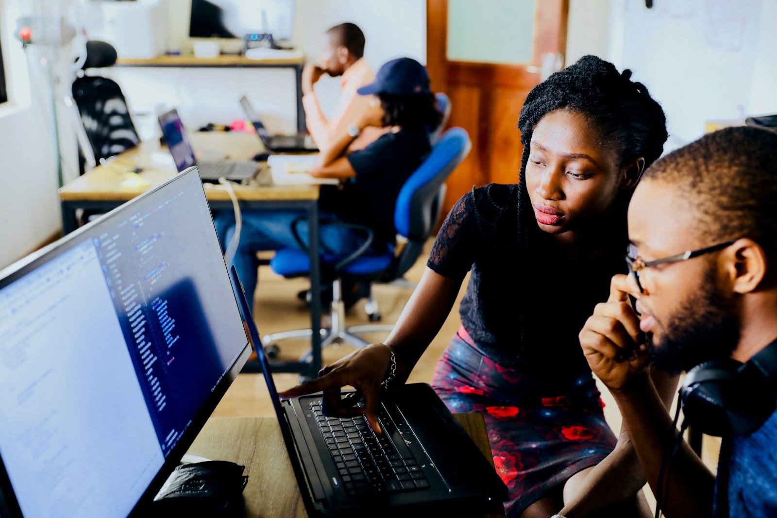 Two developers reviewing code on a laptop in an open office